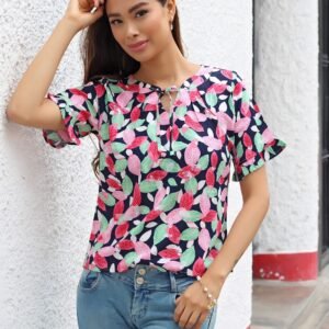 Young woman standing by a white wall wearing a vibrant floral shirt and denim jeans.