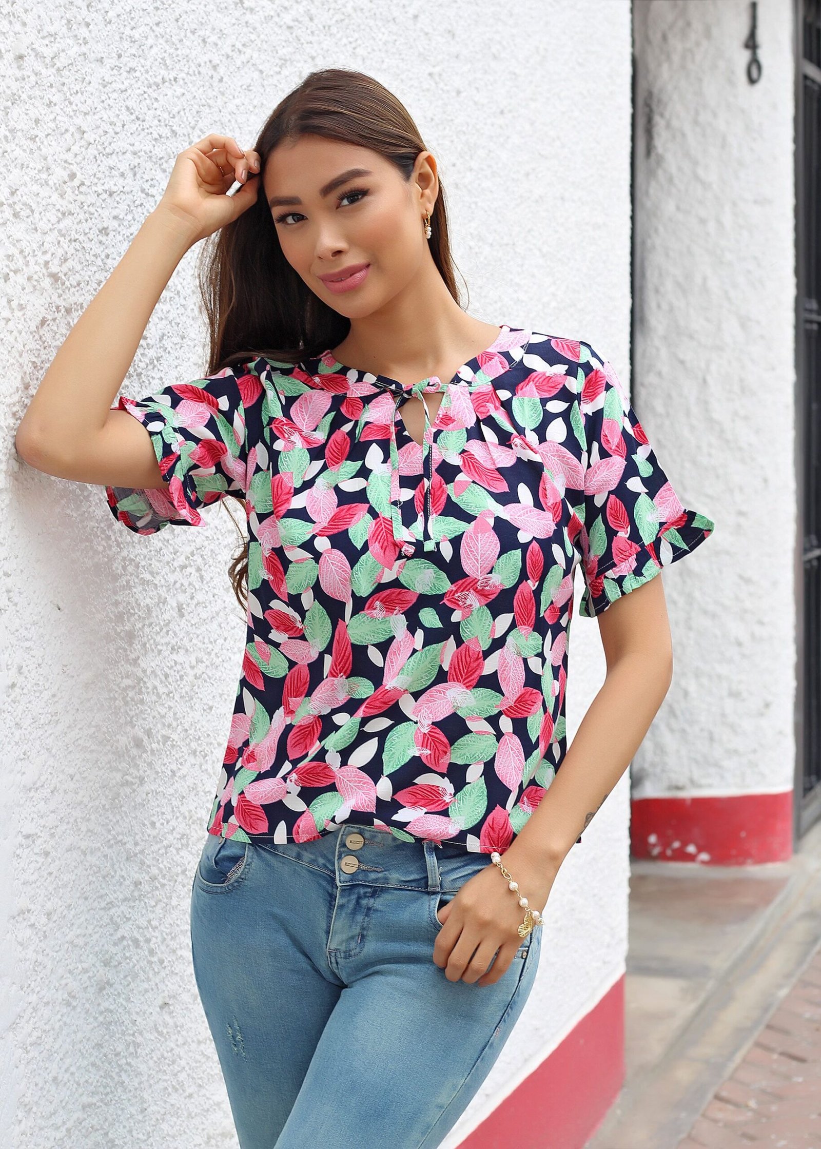 pexels photo 12846375 12846375 Young woman standing by a white wall wearing a vibrant floral shirt and denim jeans.